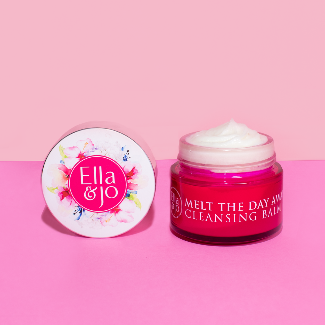 A jar of Ella & Jo Melt The Day Away Cleansing Balm placed on a pink background, with the lid beside it displaying the product name and floral design.